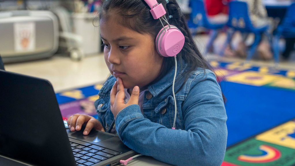 A young child with headphones uses a computer.