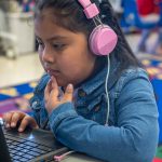A young child with headphones uses a computer.