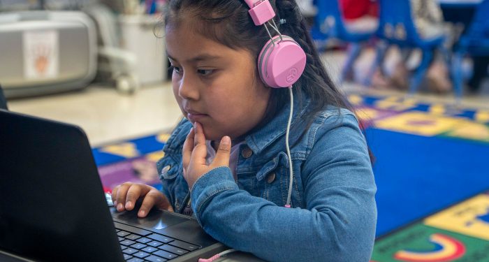 A young child with headphones uses a computer.