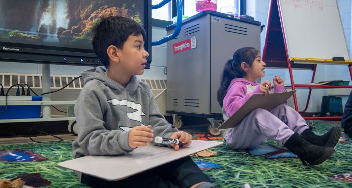 Two children sit on a carpet with dry erase board on their laps, ready to write.