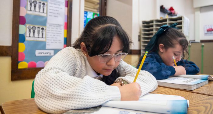 Children at desks writing in workbooks.