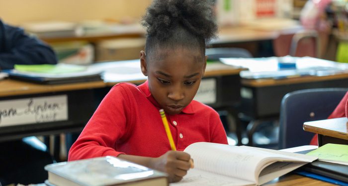 A girl in a classroom writing in a workbook.