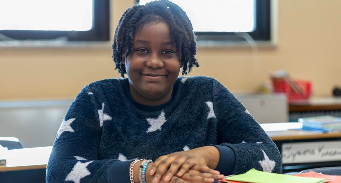 A girl at a desk, smiling.