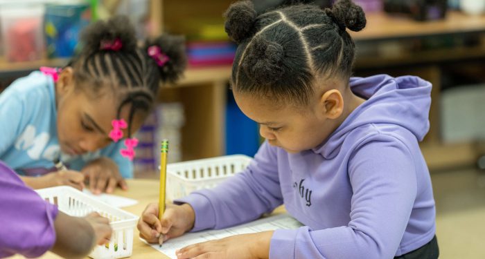 A young child writes her name at the top of a piece of paper.