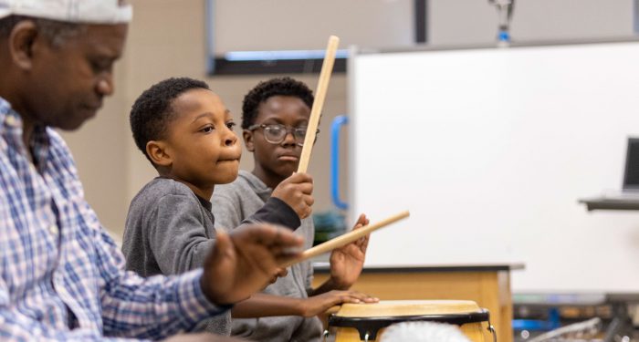 Two students and a teacher are drumming.