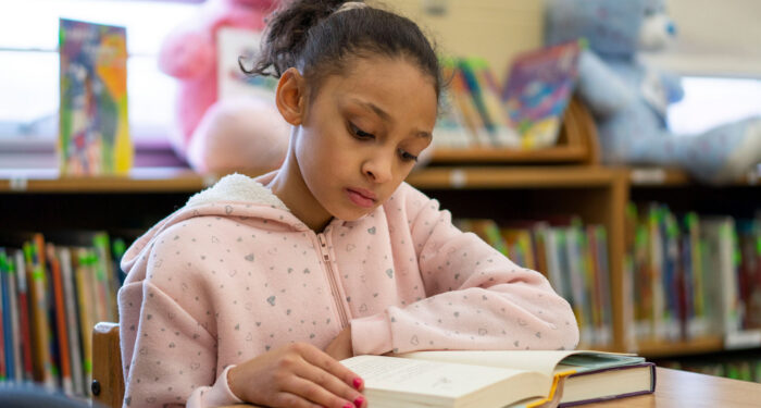 A girl in a library reading a book.