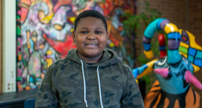 A student stands in front of a colorful mural and sculpture.