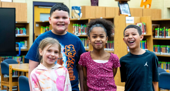 Four children stand in a library smiling.