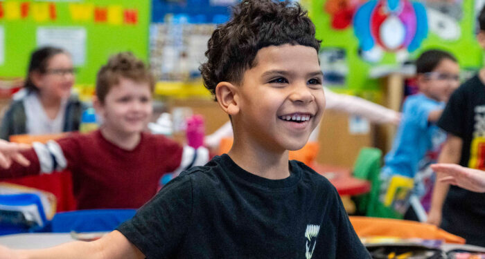 Smiling children in a classroom dancing.