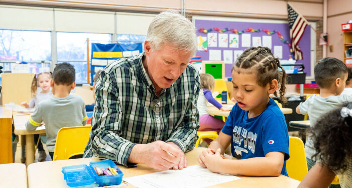 A teacher in a classroom sits at the table and helps a young student.