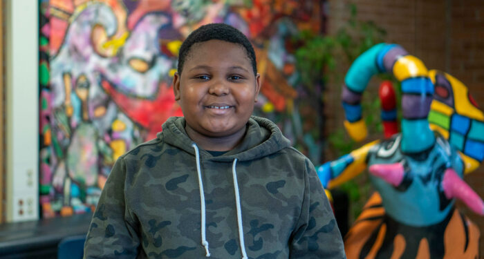 A student stands in front of a colorful mural and sculpture.