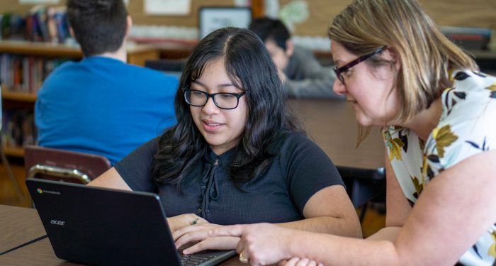 A student and teacher look at the student's computer screen.