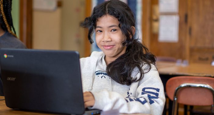 A student smiles as she uses a computer.