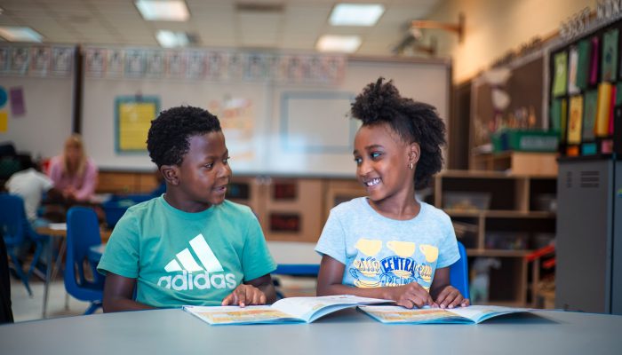 A young boy and girl smile at one another while reading.