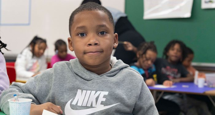 A young child in a classroom looking at the camera.