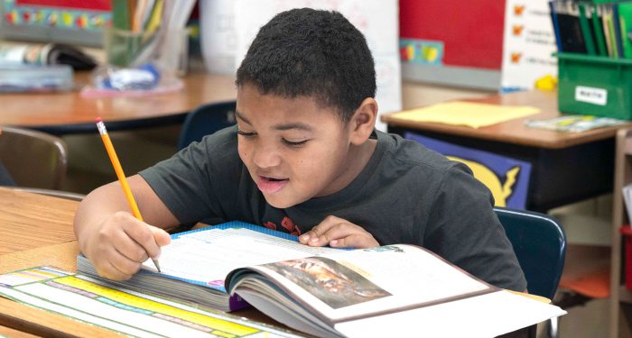 A student at a desk writing in a workbook.