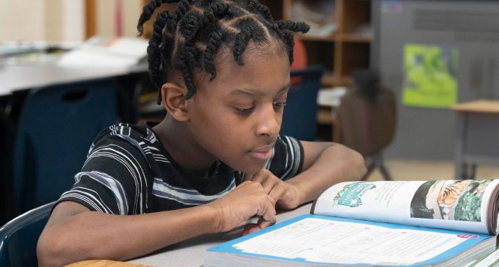 A student at a desk reading a workbook.