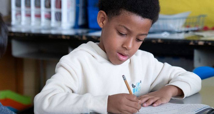 A child in a classroom writing on a worksheet.