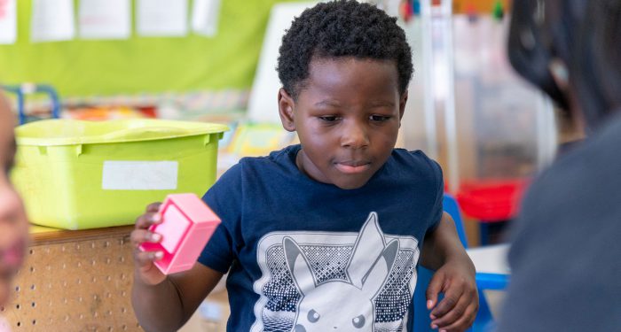 A child in a classroom holding a toy.