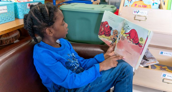 A child on a small couch looking at a picture book.