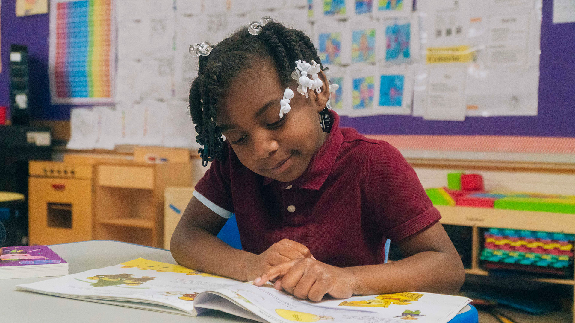 A young child points to the words of a picture book as she reads.