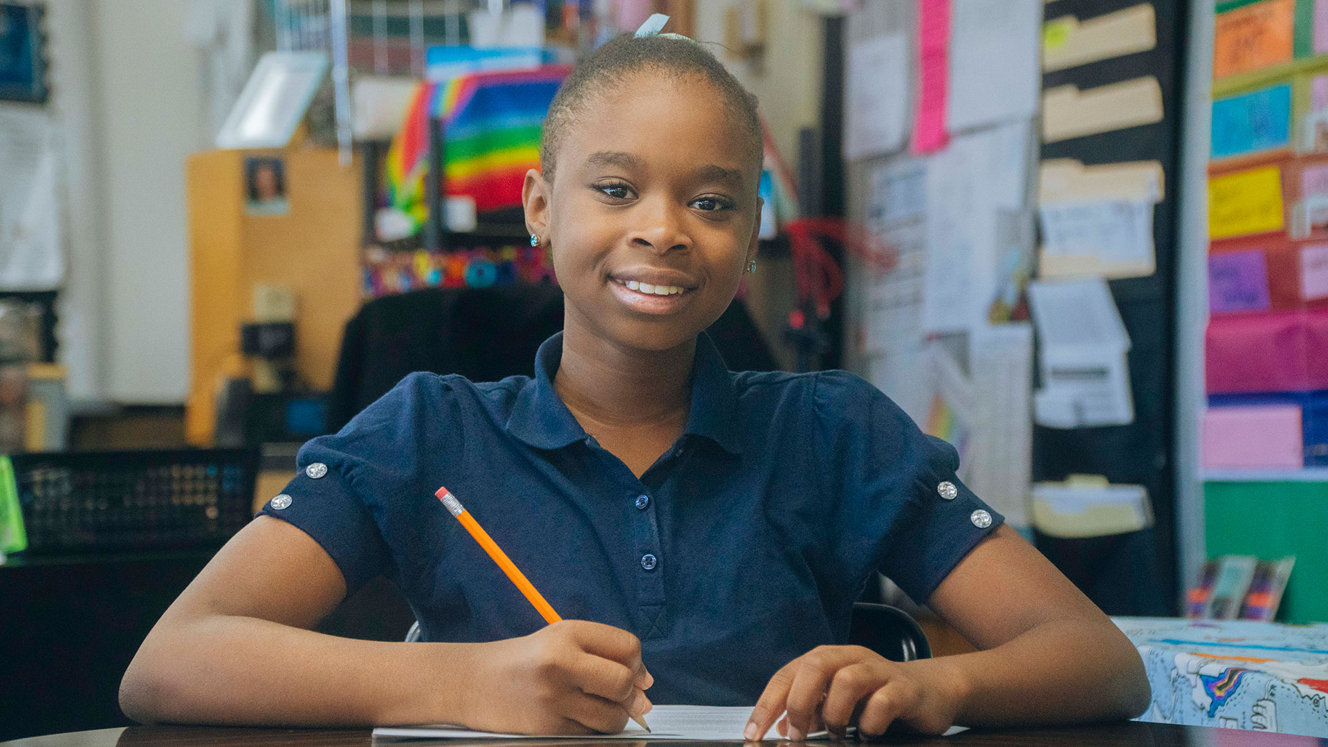 A girl at a desk holding a pencil, ready to write.