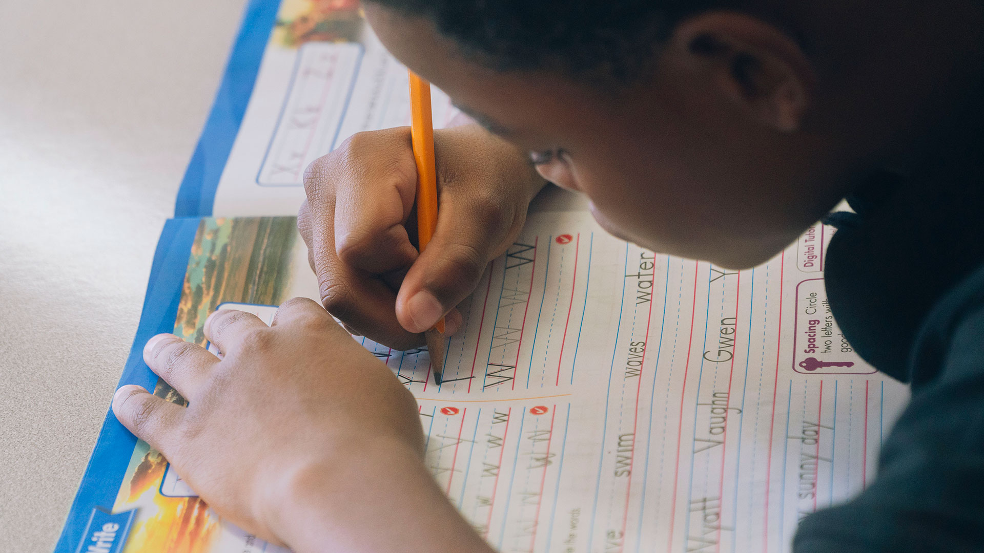 Close-up of a child practicing writing the letter 'W' in a workbook.