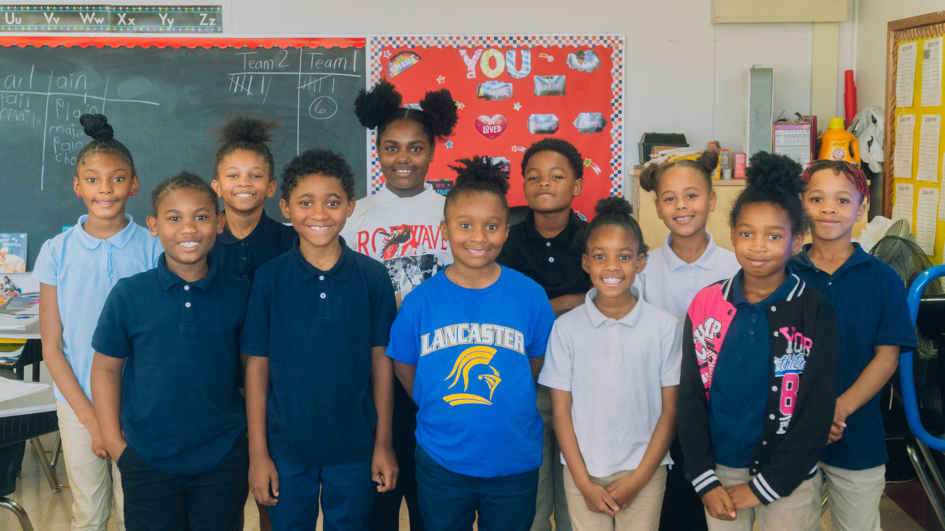 A group of children in a classroom standing in a line, smiling.