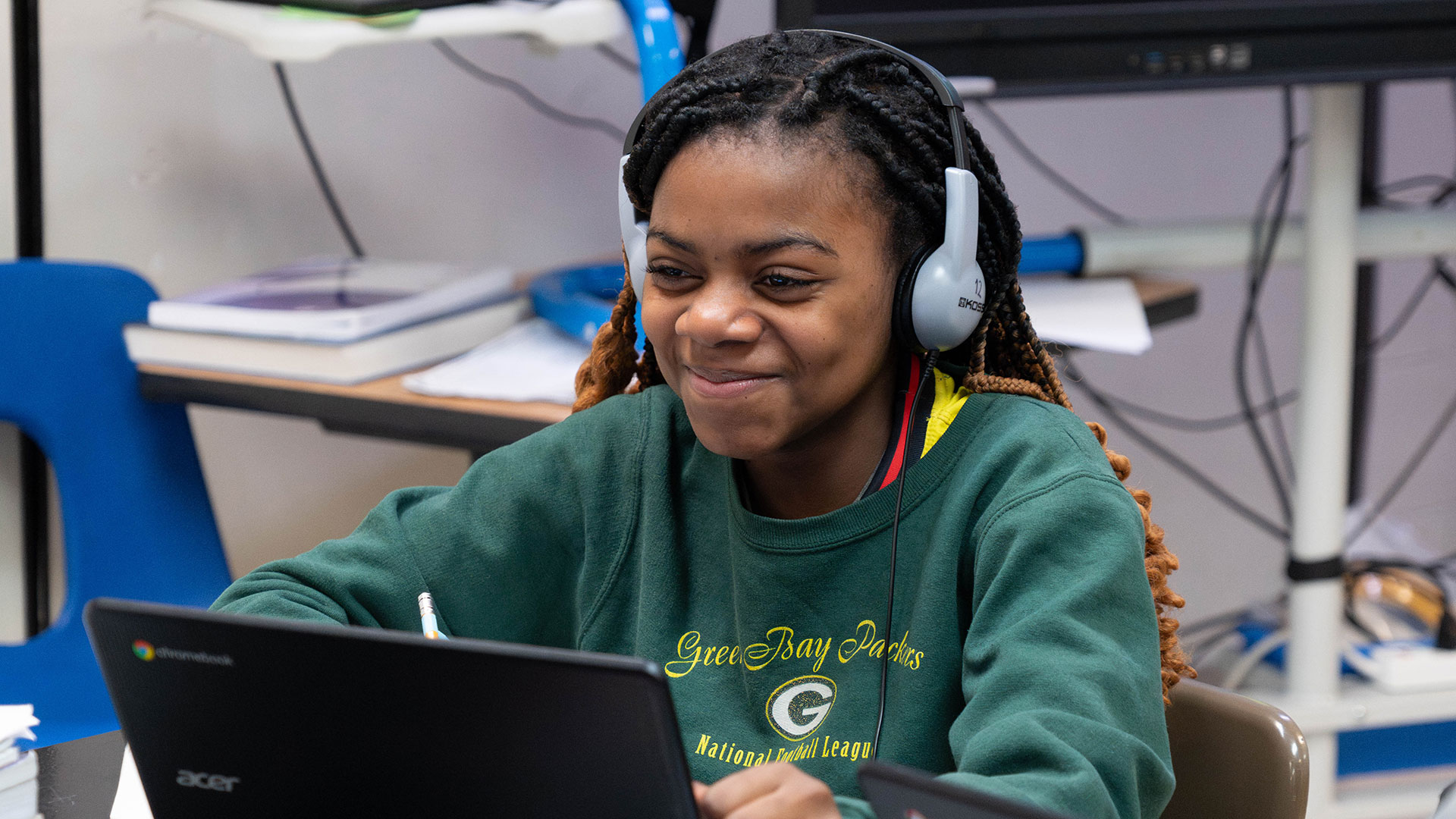 A girl with headphones uses a computer and smiles.