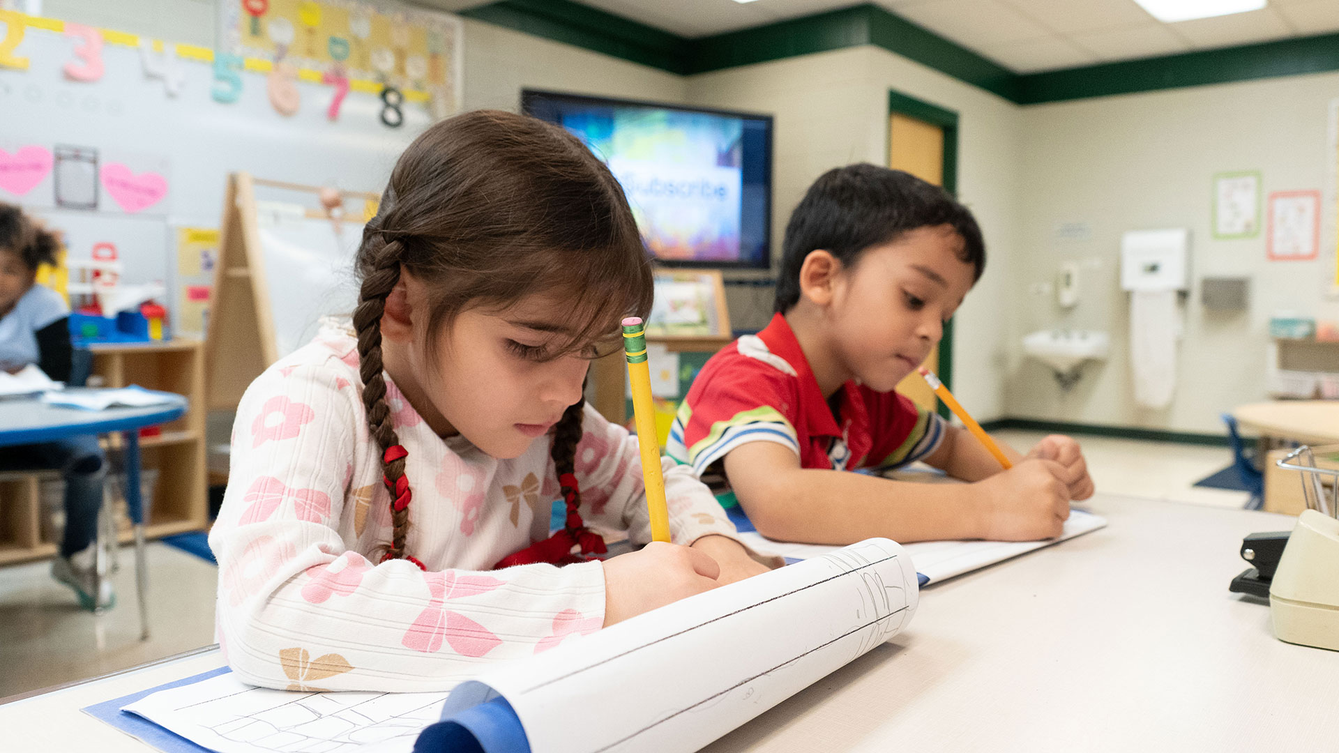 Young children in a classroom practice writing.