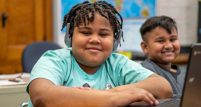 Two smiling students using computers.