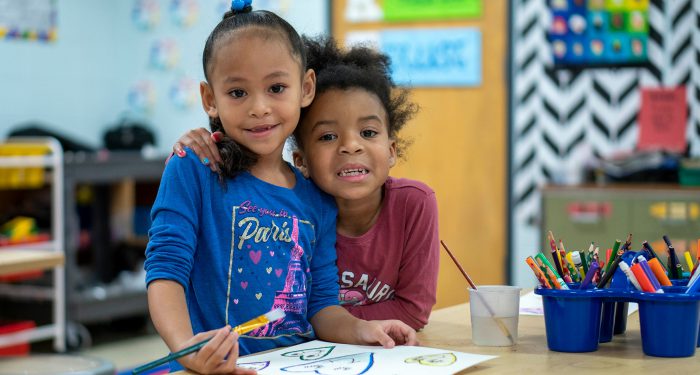 Two young girls with their arms around another.