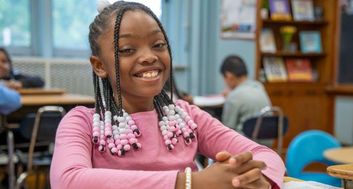 A girl at a desk smiling.
