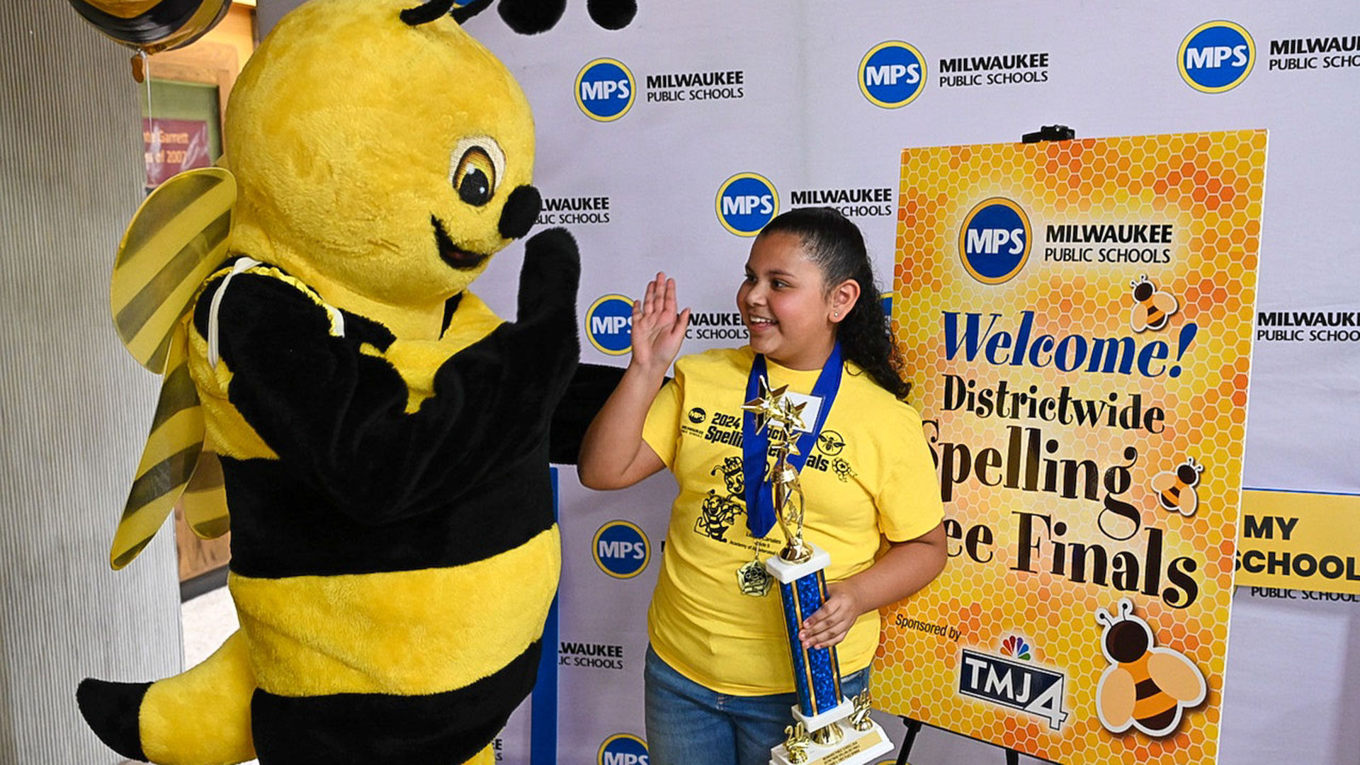 Sophia holds her trophy and high-fives the spelling bee.