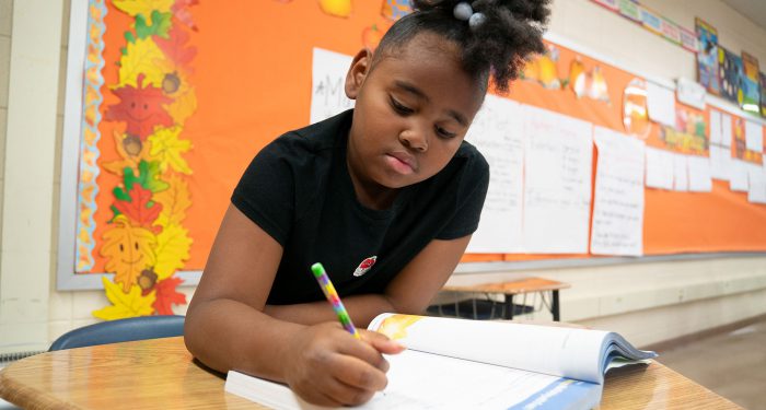 A child in a classroom writing in a workbook.
