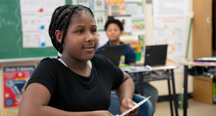 A child in a classroom holding flashcards.