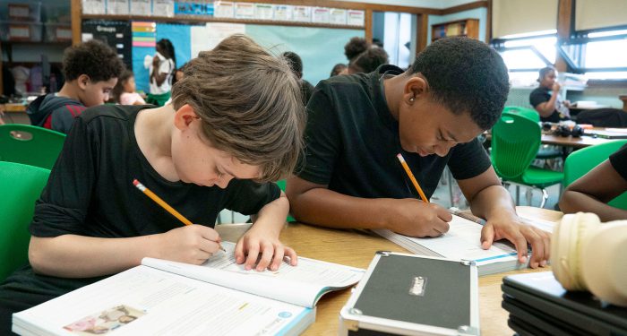 Students in a classroom writing in workbooks.