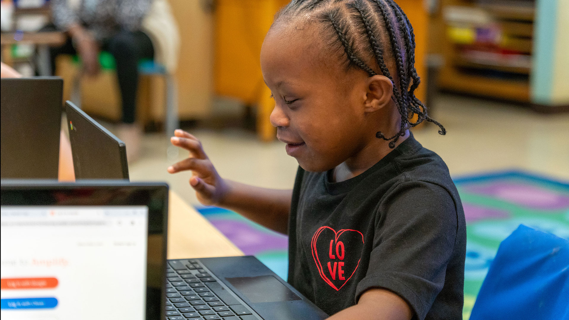 A young boy smiles as he uses a laptop.