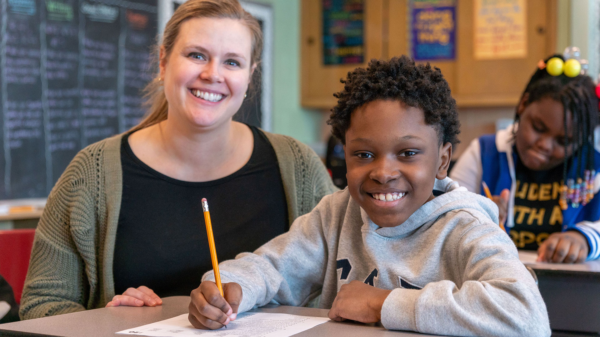 A student and teacher at a desk smiling.