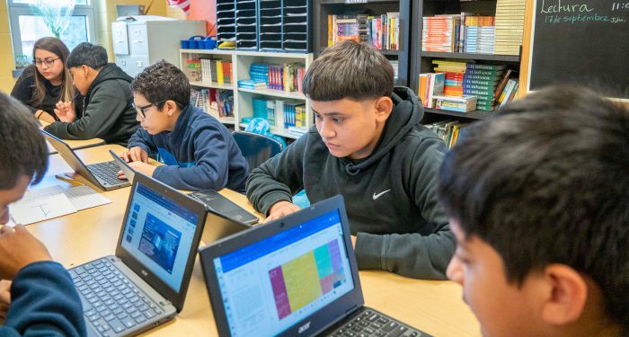 Students at a table in a classroom working on computers.