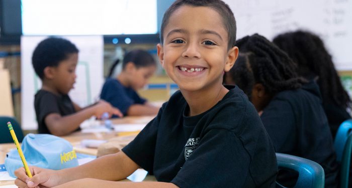 A young boy at a desk smiling.