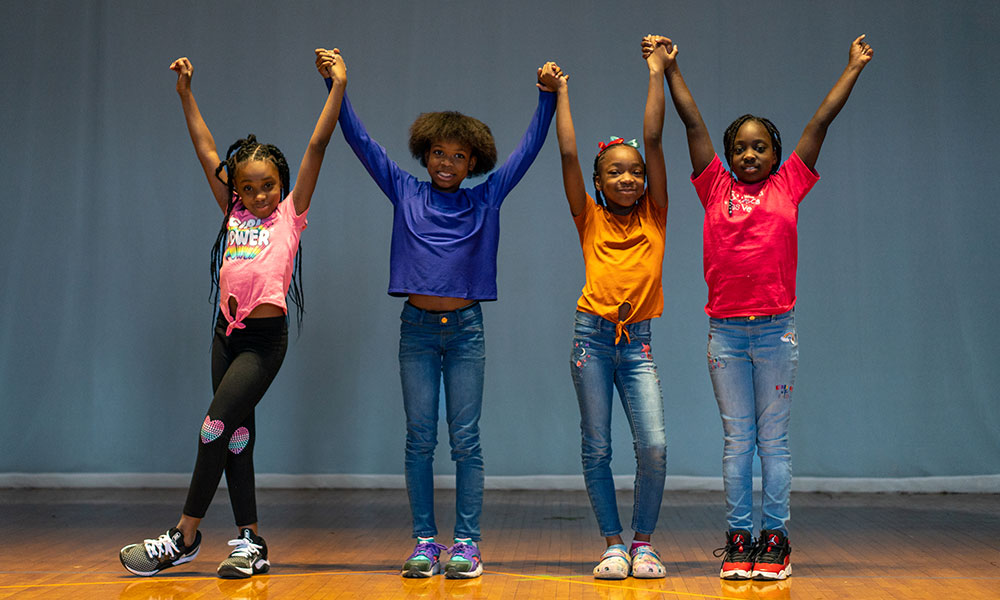 Four girls stand in a line holding their arms in the air