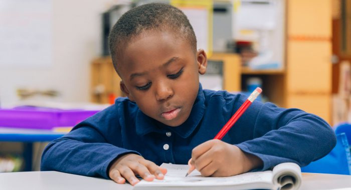 A young student concentrates as they write in a workbook.