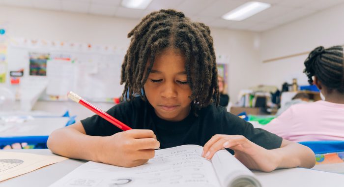 A student at a table writing in a workbook.