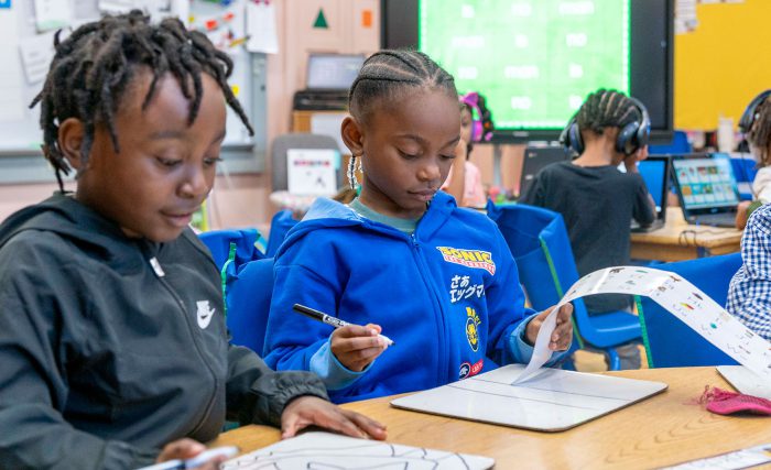 Young students in a classroom writing on whiteboards.