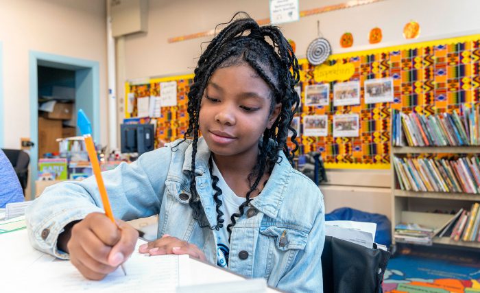 A student in a classroom writing on piece of paper.