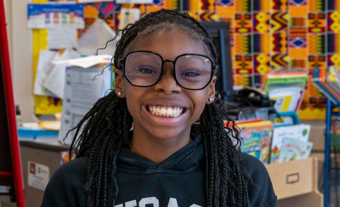 A young girl wearing big glasses with a wide smile.