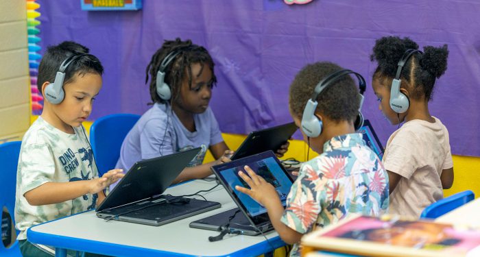 Four young students at a table play games on laptops.