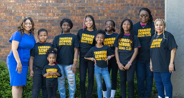 Members of the Thoreau School drama club pose in front of the school wearing matching black shirts.