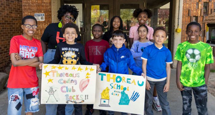 The Thoreau School coding club stand in front of the school with handmade club signs.